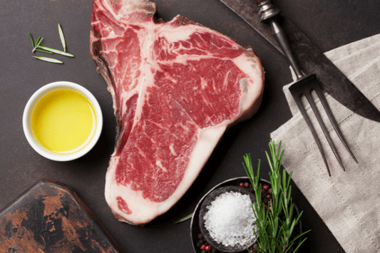 Raw T-bone steak with olive oil, rosemary, salt, and pepper on a dark kitchen surface