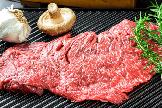 Raw flap meat steak on grill pan with garlic, mushroom, and rosemary