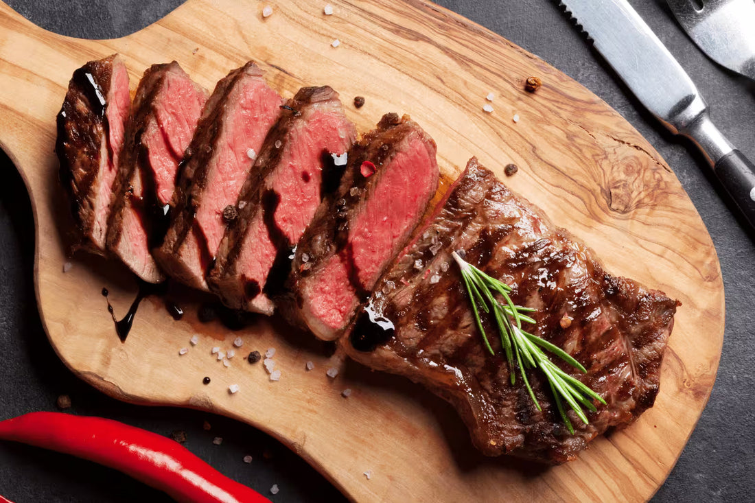 Raw striploin steak seasoned with rosemary and sea salt beside garlic and olive oil