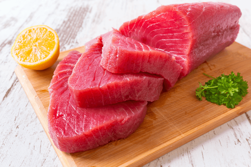 Raw tuna steaks on a wooden cutting board with lemon and parsley