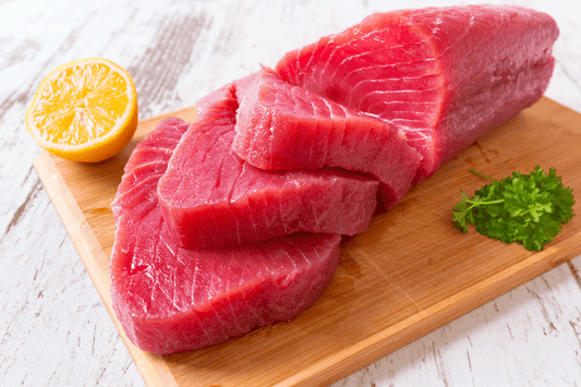 Raw tuna steaks on a wooden cutting board with lemon and parsley