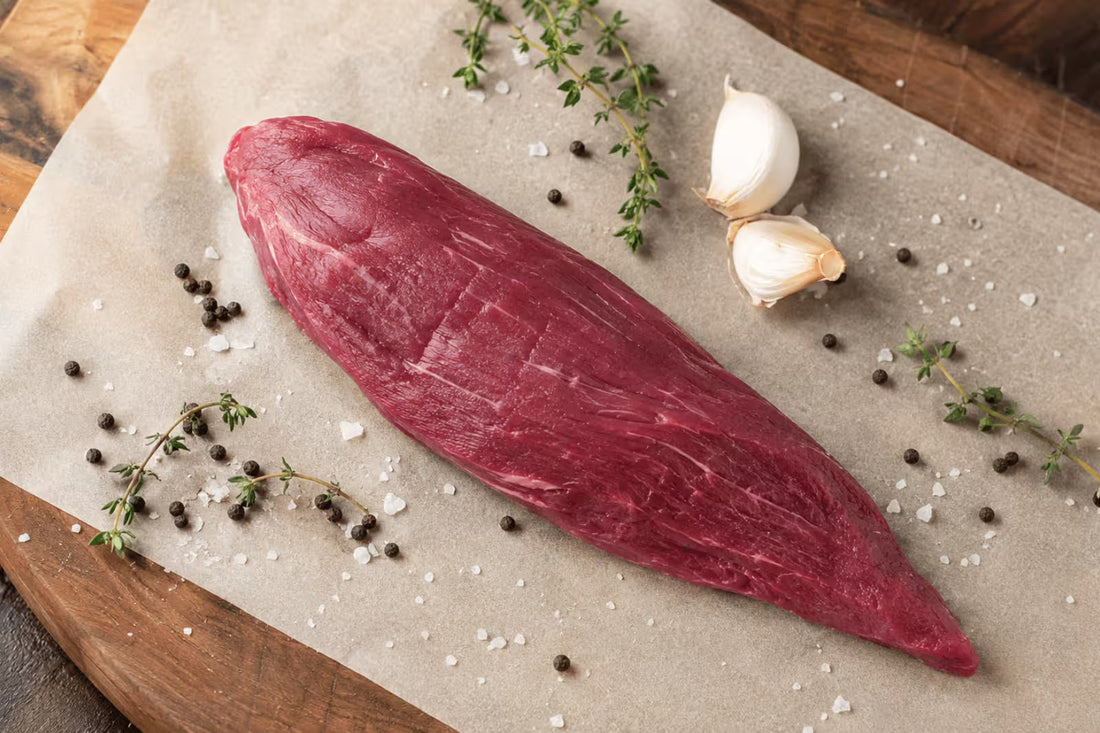 Raw whole teres major steak with thyme, garlic, salt, and pepper on parchment paper